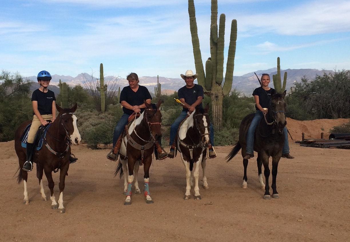 Four horses with riders posing in front of cactus.