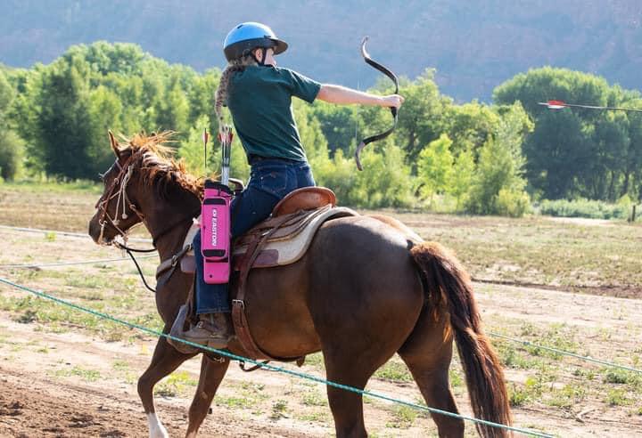 Horseback rider shooting arrow at target while horse is galloping